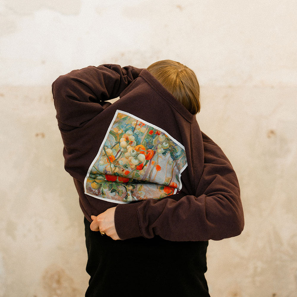 Person wearing a sweatshirt with a colorful poster against a beige wall.