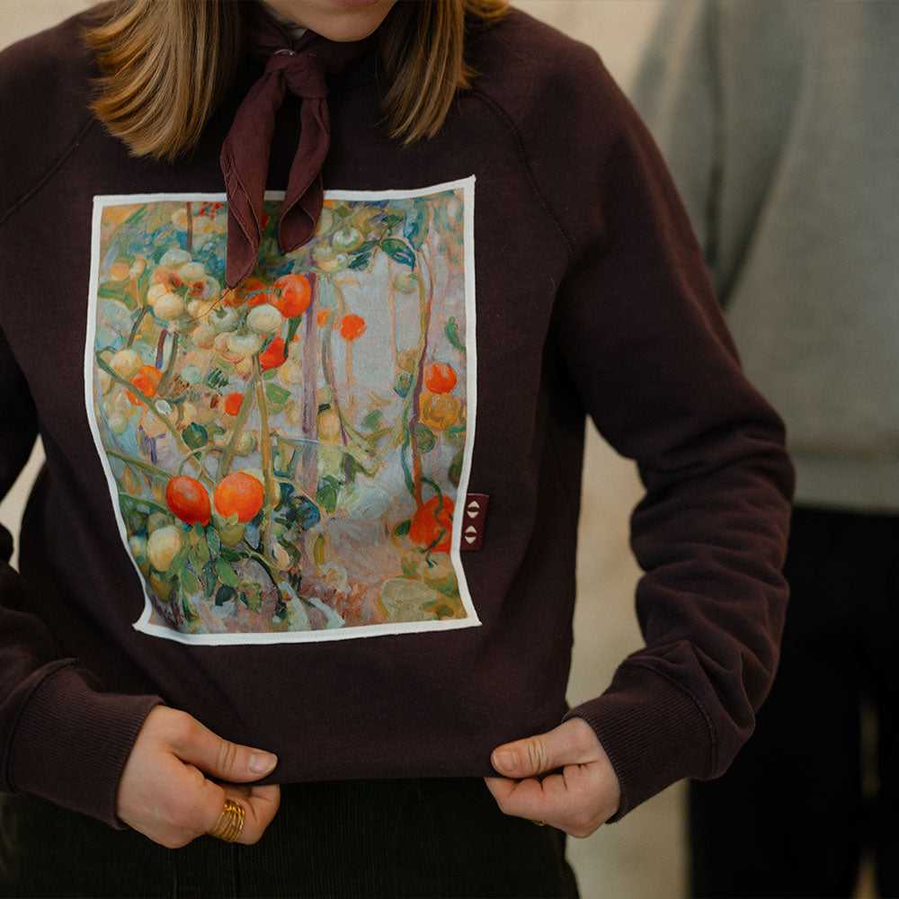 Person wearing a brown sweatshirt with a printed design of a garden scene.